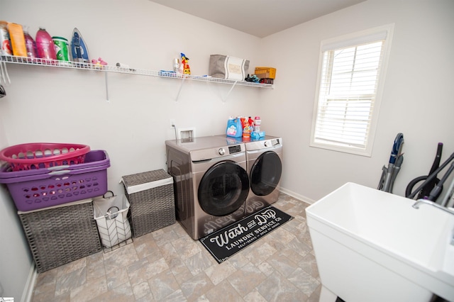 clothes washing area featuring washing machine and clothes dryer, a sink, stone finish flooring, baseboards, and laundry area