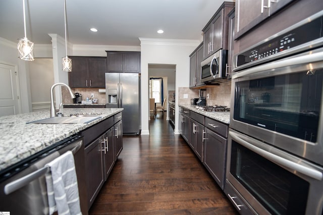 kitchen featuring stainless steel appliances, a sink, dark brown cabinets, light stone countertops, and ornamental molding