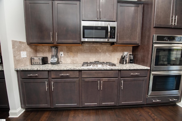 kitchen with backsplash, appliances with stainless steel finishes, dark brown cabinetry, and dark wood-style flooring