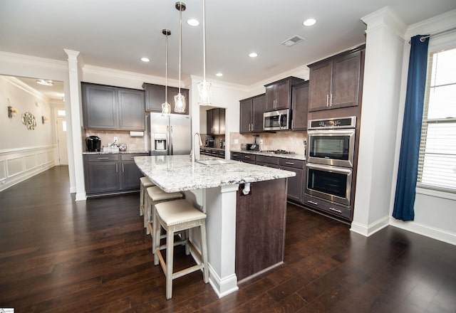 kitchen featuring a breakfast bar, a kitchen island with sink, dark brown cabinetry, stainless steel appliances, and visible vents