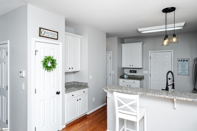kitchen with light stone counters, a kitchen breakfast bar, a sink, white cabinets, and dark wood-style floors