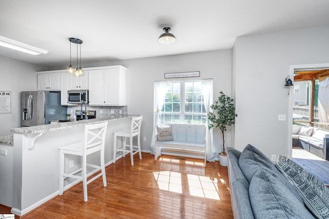 kitchen with a breakfast bar, stainless steel appliances, light wood-style flooring, white cabinets, and a peninsula