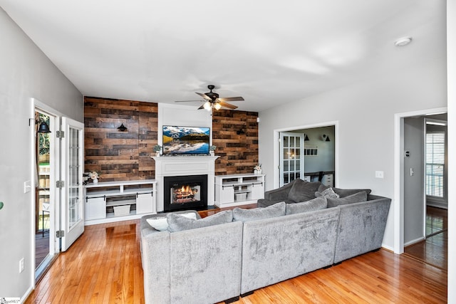 living area with ceiling fan, a warm lit fireplace, wood walls, and wood finished floors