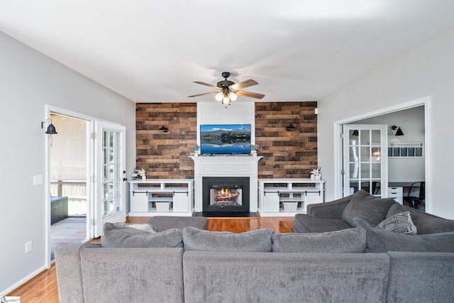 living area featuring a fireplace with flush hearth, a ceiling fan, and wood finished floors