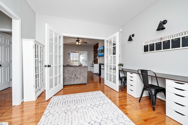 office space with french doors, a fireplace, light wood-style floors, and a ceiling fan
