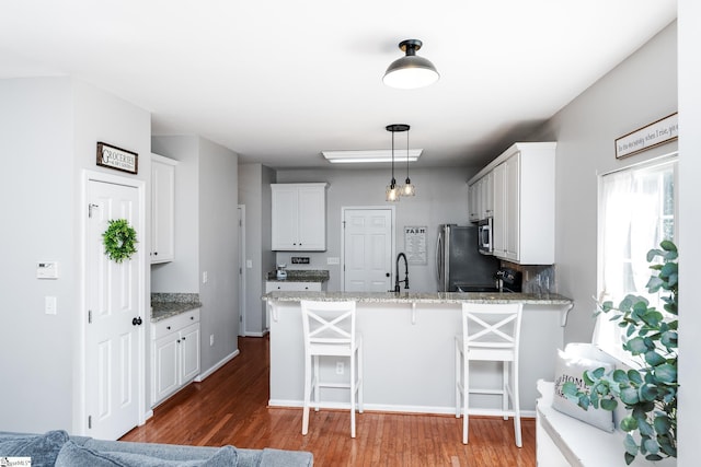 kitchen featuring dark wood finished floors, a kitchen breakfast bar, stainless steel appliances, a peninsula, and white cabinetry