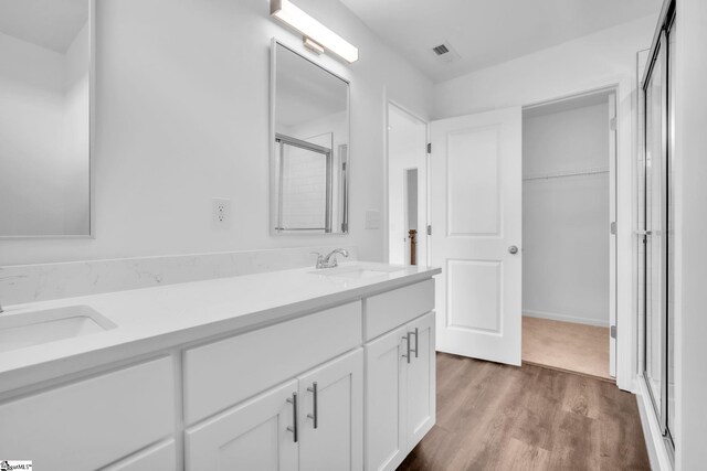 full bath featuring wood finished floors, a sink, double vanity, and a stall shower