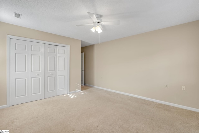 unfurnished bedroom featuring baseboards, visible vents, light colored carpet, a ceiling fan, and a closet
