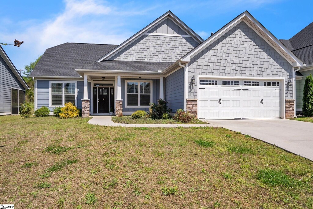 craftsman inspired home featuring concrete driveway, a front lawn, stone siding, an attached garage, and roof with shingles