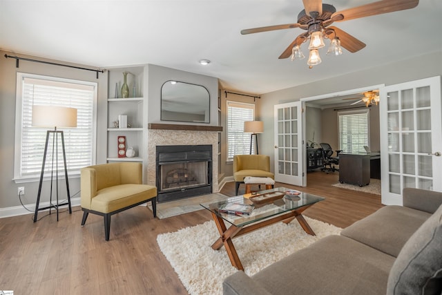 living room featuring wood finished floors, ceiling fan, french doors, a tile fireplace, and baseboards