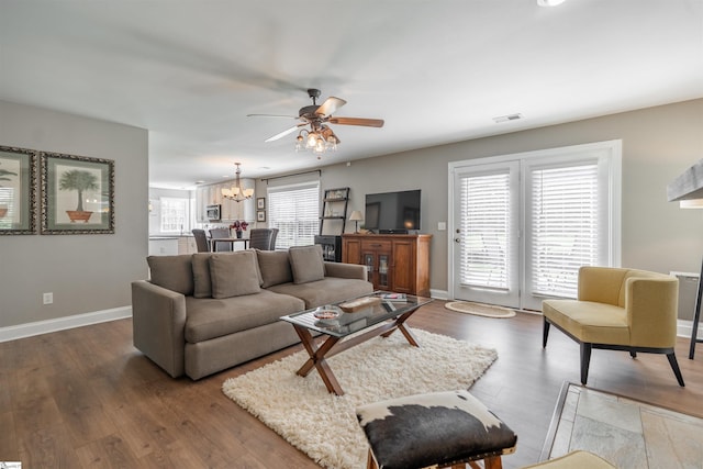 living area featuring ceiling fan with notable chandelier, baseboards, wood finished floors, and visible vents