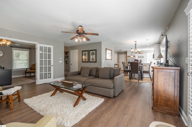 living area with baseboards, french doors, wood finished floors, and ceiling fan with notable chandelier