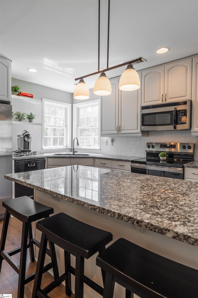kitchen featuring backsplash, a kitchen bar, appliances with stainless steel finishes, and dark stone countertops