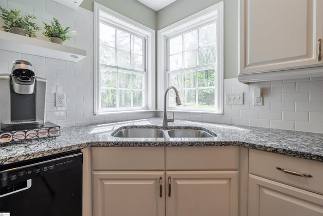 kitchen featuring stone counters, dishwasher, a sink, and tasteful backsplash