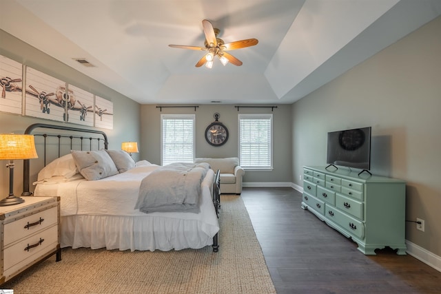 bedroom with baseboards, visible vents, a ceiling fan, dark wood-type flooring, and a raised ceiling