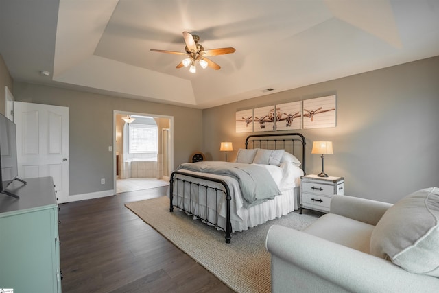 bedroom with a tray ceiling, wood finished floors, visible vents, connected bathroom, and baseboards