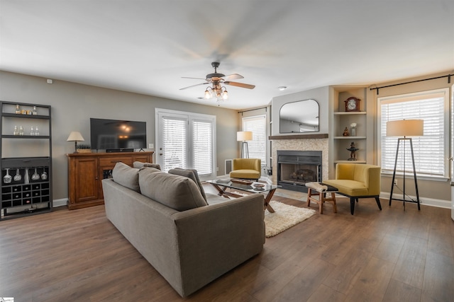 living room featuring baseboards, a ceiling fan, dark wood-style flooring, and a fireplace
