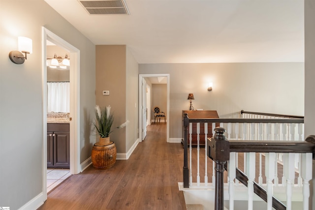 corridor with baseboards, wood finished floors, visible vents, and an upstairs landing