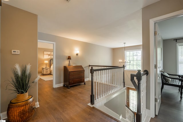 hall with a chandelier, wood finished floors, baseboards, and an upstairs landing