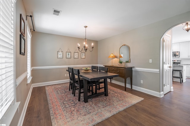 dining space featuring an inviting chandelier, visible vents, dark wood-type flooring, arched walkways, and baseboards