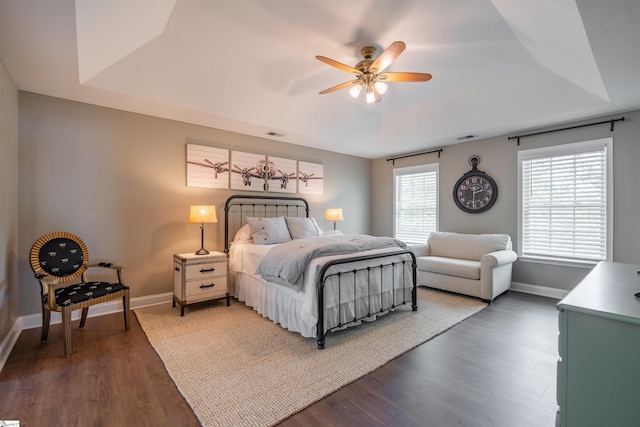 bedroom featuring a raised ceiling, baseboards, and dark wood-style flooring