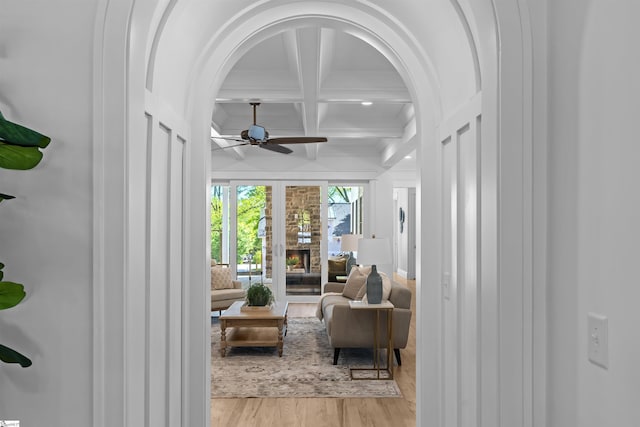 interior space with beam ceiling, arched walkways, light wood-type flooring, coffered ceiling, and a ceiling fan