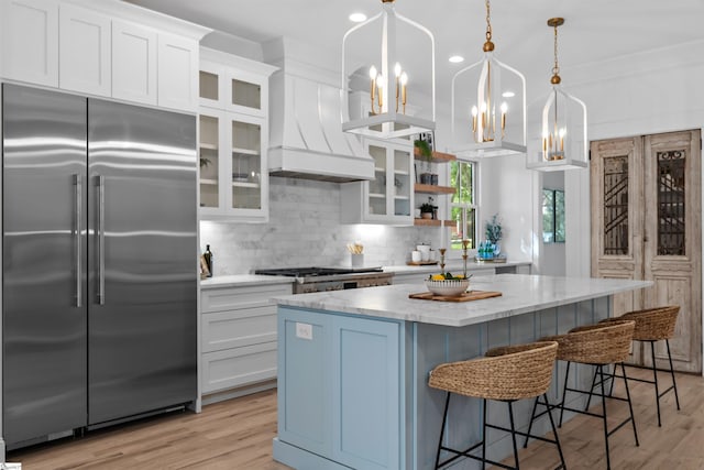 kitchen with a notable chandelier, decorative backsplash, built in fridge, custom exhaust hood, and white cabinetry
