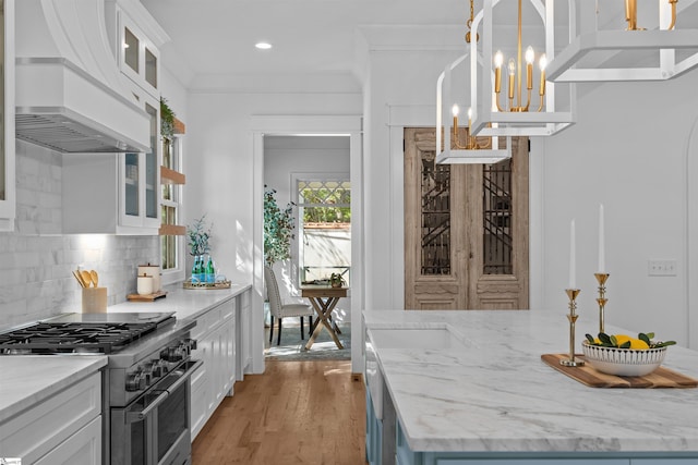 kitchen featuring white cabinets, high end stainless steel range, backsplash, light wood-style flooring, and custom range hood