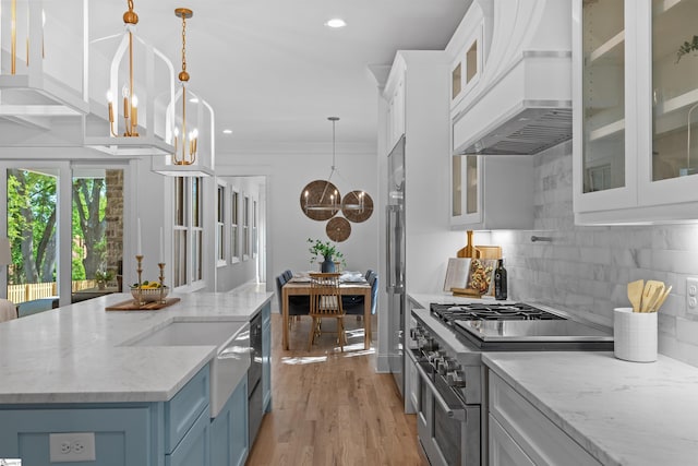 kitchen featuring white cabinets, custom exhaust hood, premium appliances, backsplash, and a notable chandelier