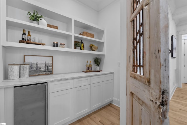 bar featuring light wood-style flooring, baseboards, refrigerator, and crown molding