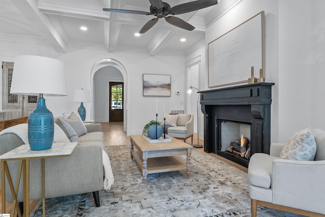 living area featuring wood finished floors, arched walkways, a lit fireplace, coffered ceiling, and beam ceiling