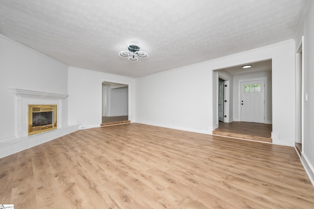 unfurnished living room featuring ornamental molding, light wood-type flooring, baseboards, a fireplace, and a textured ceiling
