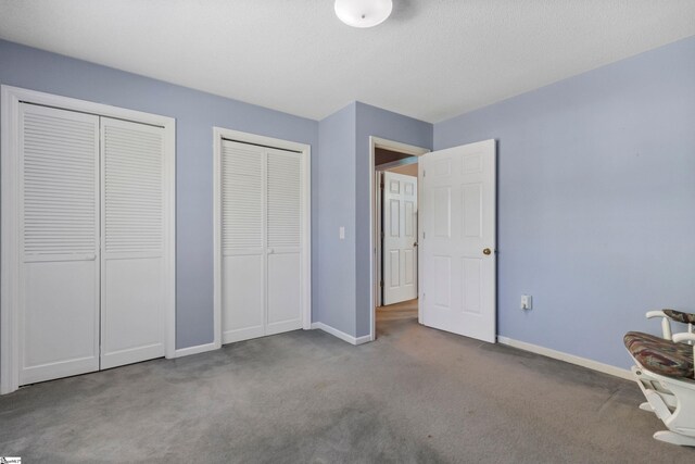 unfurnished bedroom featuring baseboards, carpet flooring, and multiple closets