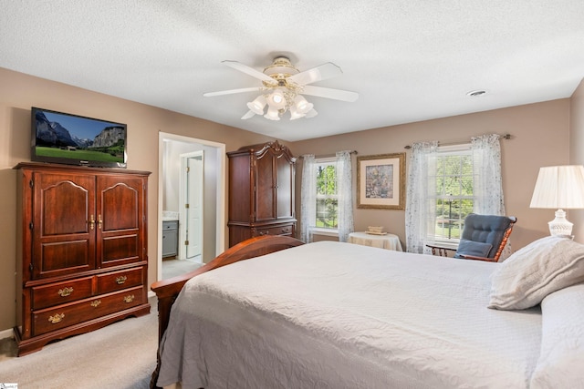 bedroom with a ceiling fan, connected bathroom, a textured ceiling, and light colored carpet