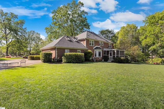 view of front of house with a front yard, a sunroom, and brick siding