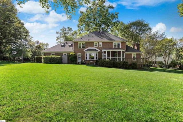 georgian-style home featuring a sunroom, a chimney, and a front lawn