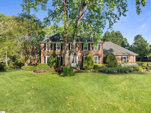 colonial inspired home with brick siding and a front yard