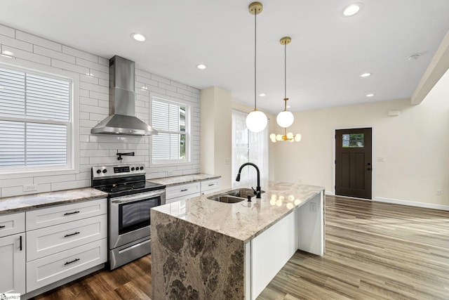 kitchen with a sink, stainless steel range with electric cooktop, a center island with sink, dark wood finished floors, and wall chimney exhaust hood