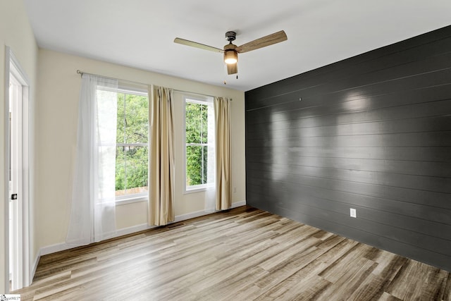 spare room featuring baseboards, wooden walls, wood finished floors, and ceiling fan