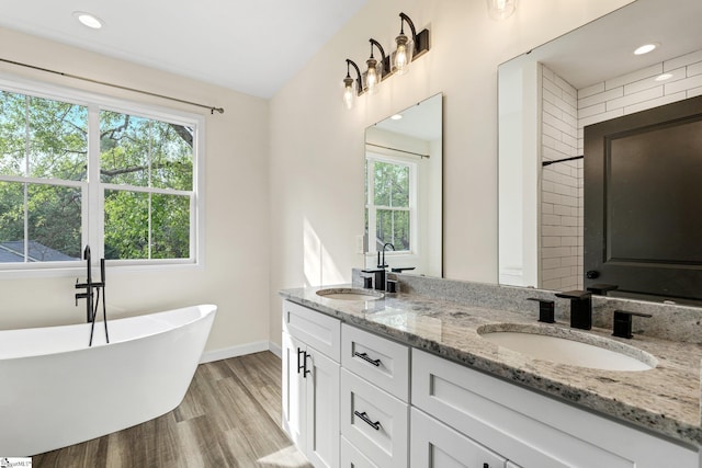 full bathroom featuring a soaking tub, baseboards, wood finished floors, and a sink