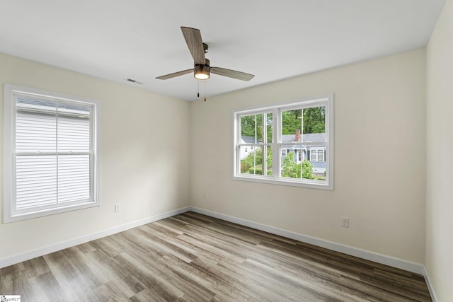 unfurnished room featuring baseboards, wood finished floors, visible vents, and ceiling fan