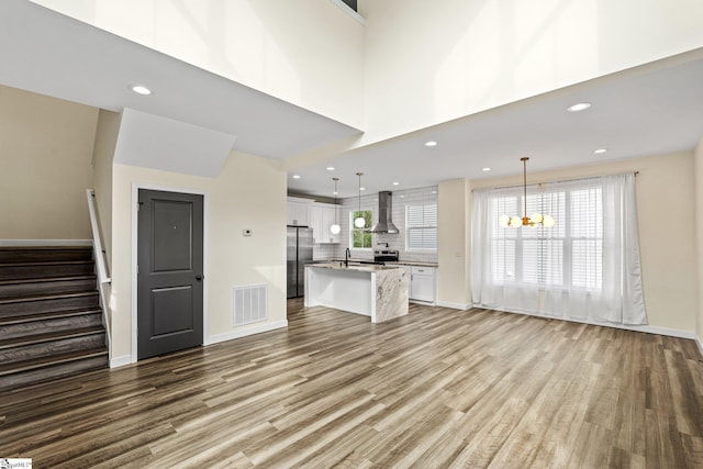 unfurnished living room featuring baseboards, visible vents, a chandelier, wood finished floors, and stairway