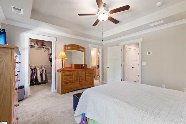 bedroom with a closet, a walk in closet, a raised ceiling, carpet flooring, and visible vents