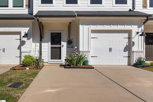 view of exterior entry featuring an attached garage, driveway, and a shingled roof