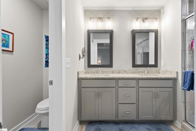 bathroom featuring double vanity, a shower stall, toilet, and a sink