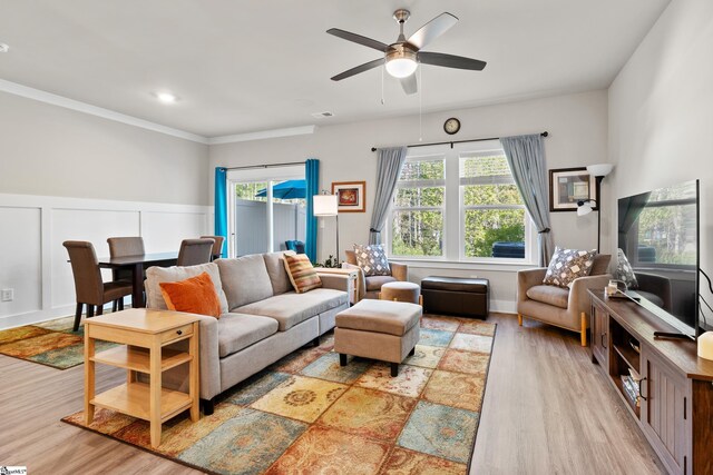 living area with wood finished floors, visible vents, ornamental molding, wainscoting, and ceiling fan
