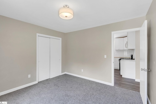 unfurnished bedroom featuring dark carpet, a closet, and baseboards