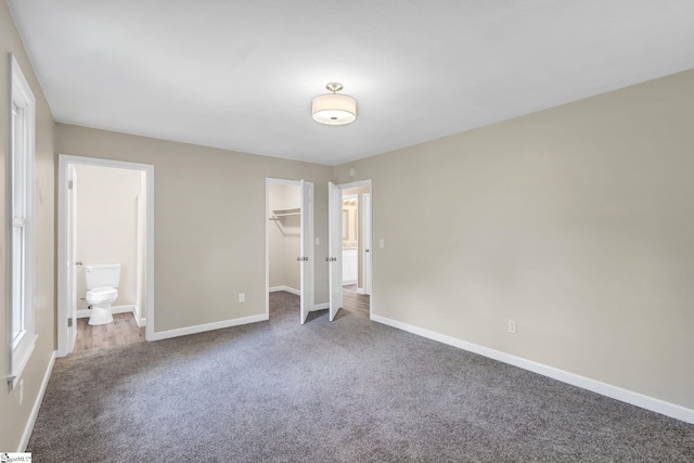 unfurnished bedroom featuring a walk in closet, carpet flooring, baseboards, and ensuite bathroom