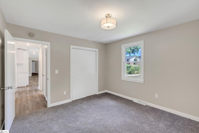 unfurnished bedroom featuring visible vents, light carpet, baseboards, and a closet