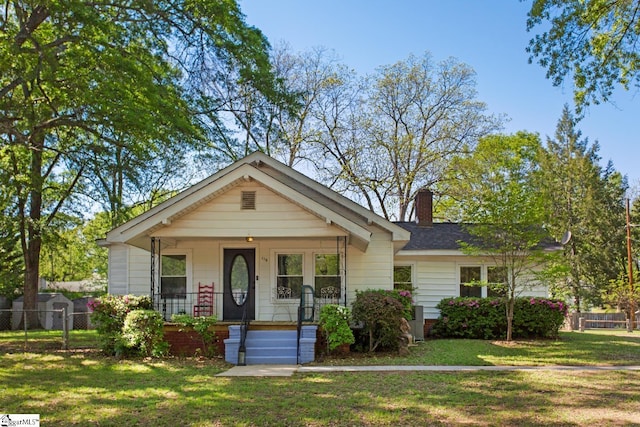 bungalow featuring a chimney, a front lawn, covered porch, and fence